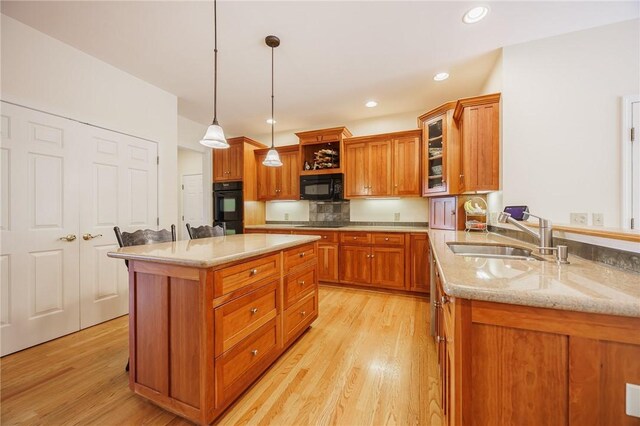 kitchen with brown cabinets, a sink, light stone counters, black appliances, and light wood-style floors