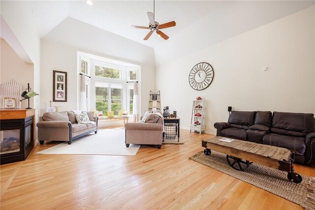 living area with light wood-style floors, a multi sided fireplace, vaulted ceiling, and a ceiling fan