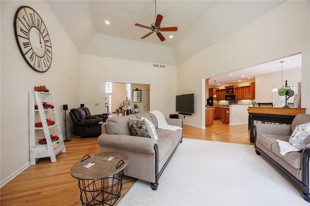 living area with a ceiling fan, visible vents, light wood-type flooring, baseboards, and a high ceiling