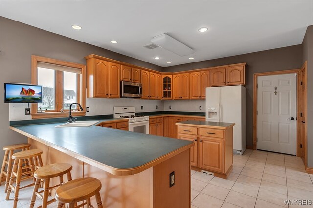 kitchen featuring a kitchen bar, visible vents, a sink, white appliances, and light tile patterned flooring