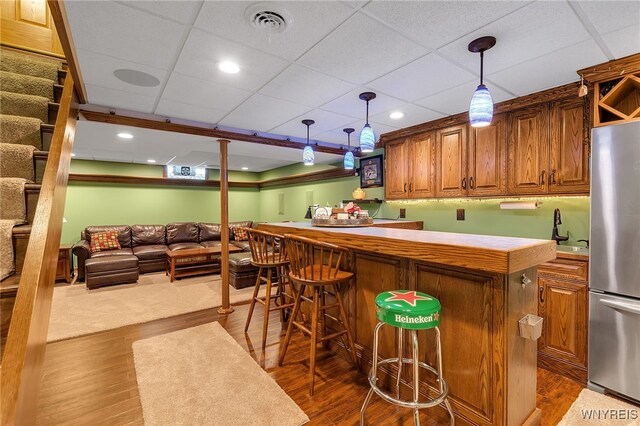 bar with dark wood-style flooring, decorative light fixtures, a sink, freestanding refrigerator, and indoor bar
