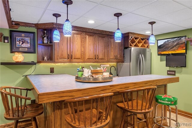 bar featuring freestanding refrigerator, pendant lighting, and a drop ceiling