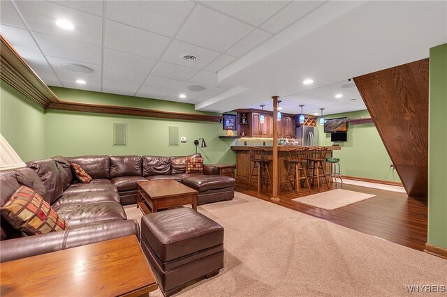 living room featuring carpet floors, wood finished floors, baseboards, a paneled ceiling, and bar area