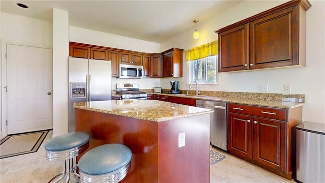 kitchen with light stone counters, appliances with stainless steel finishes, a sink, a center island, and a kitchen bar