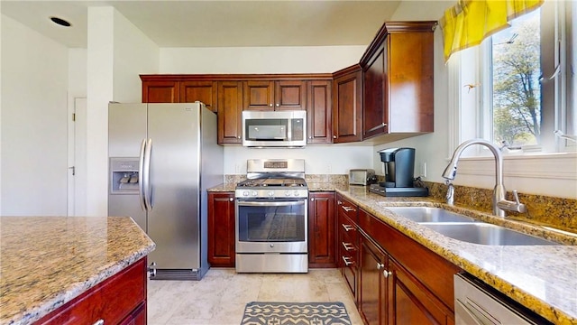 kitchen with light stone counters, a sink, dark brown cabinets, and stainless steel appliances