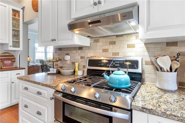 kitchen with glass insert cabinets, under cabinet range hood, white cabinetry, and gas range