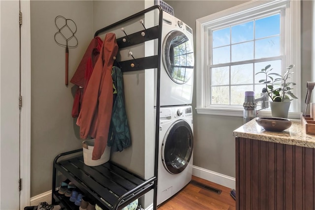 clothes washing area featuring baseboards, stacked washer and clothes dryer, light wood-style flooring, and laundry area