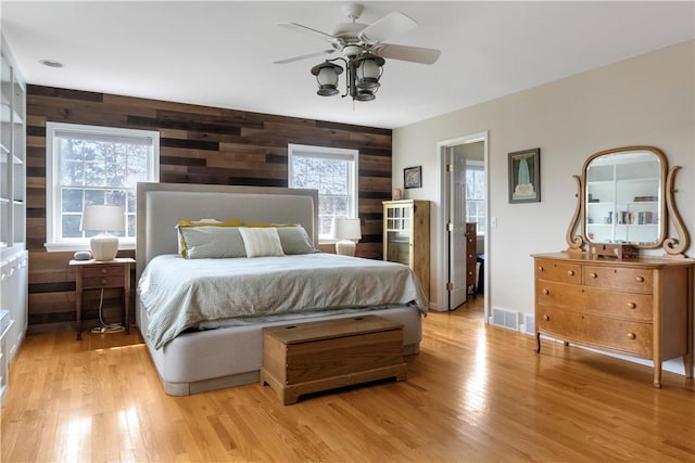 bedroom featuring wooden walls, ceiling fan, visible vents, and light wood-style floors