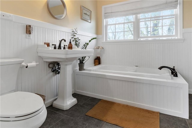 full bathroom featuring a wainscoted wall, tile patterned flooring, a garden tub, and toilet