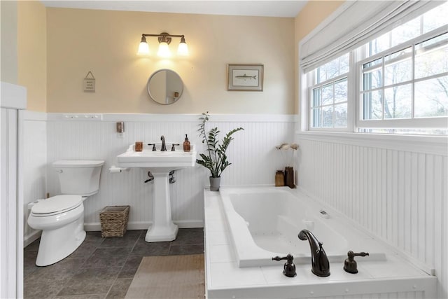 bathroom with a bath, tile patterned flooring, wainscoting, a sink, and toilet