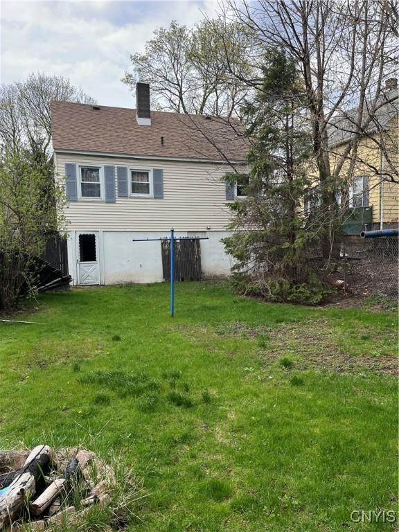 rear view of property featuring a lawn, a chimney, and central air condition unit