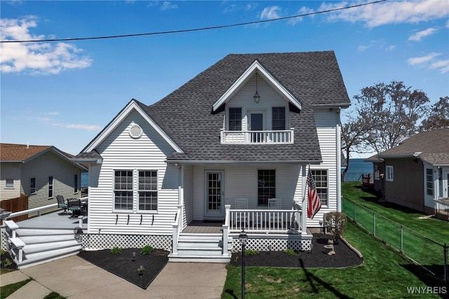 view of front of property with a front yard, roof with shingles, a wooden deck, fence, and a balcony