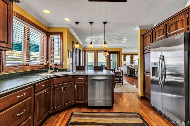 kitchen with dark countertops, dark wood finished floors, a sink, ornamental molding, and stainless steel appliances