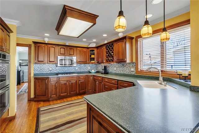 kitchen with a sink, stainless steel appliances, decorative light fixtures, tasteful backsplash, and ornamental molding
