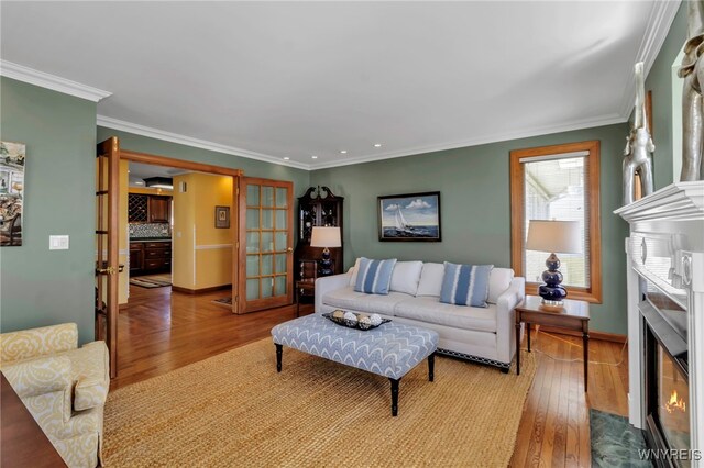 living area with a fireplace with flush hearth, crown molding, and hardwood / wood-style flooring