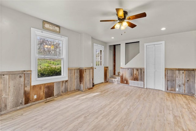 unfurnished room featuring visible vents, wood walls, wood finished floors, a wainscoted wall, and a ceiling fan