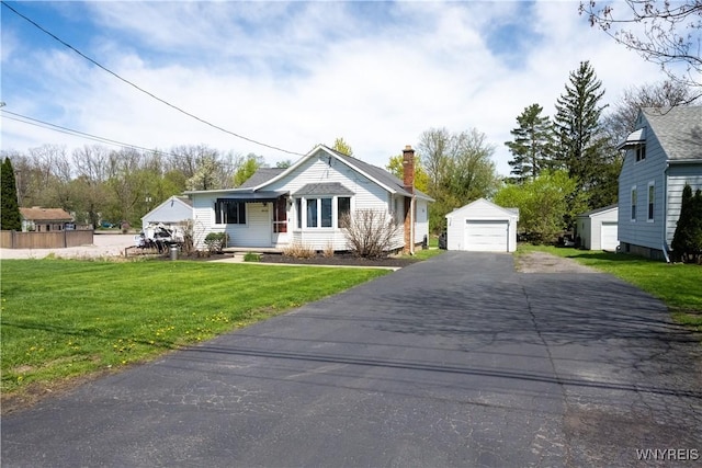 bungalow-style house with an outdoor structure, aphalt driveway, a front yard, a chimney, and a detached garage