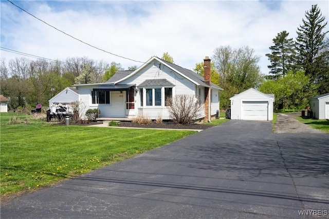 bungalow-style house featuring a garage, a front yard, a chimney, an outdoor structure, and driveway