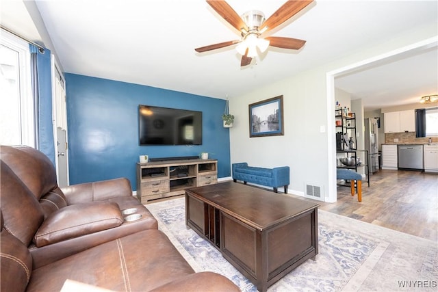living area featuring visible vents, light wood-style flooring, ceiling fan, and baseboards