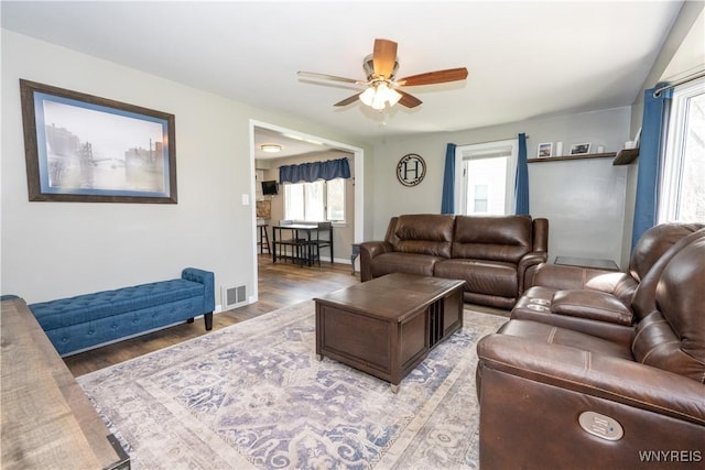 living area with visible vents, a ceiling fan, baseboards, and wood finished floors