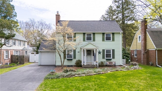 colonial inspired home featuring fence, roof with shingles, aphalt driveway, a front yard, and a chimney