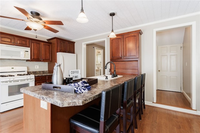 kitchen with white appliances, a kitchen breakfast bar, hanging light fixtures, and light wood-style flooring