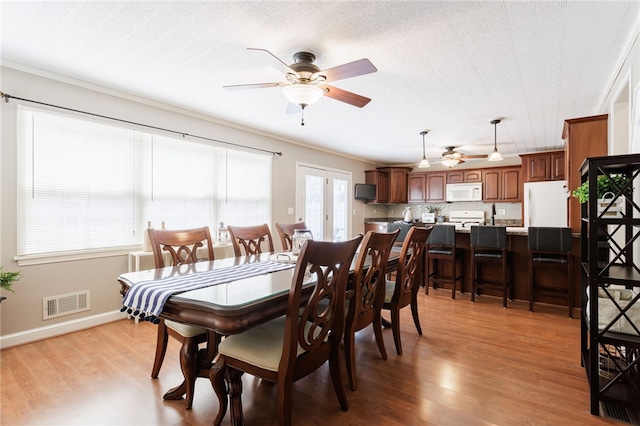 dining room featuring crown molding, a ceiling fan, baseboards, wood finished floors, and visible vents