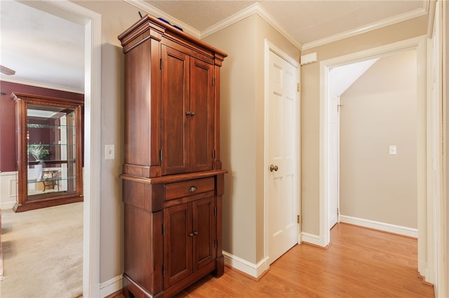 hall with light wood-type flooring, ornamental molding, and baseboards