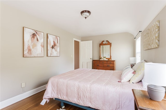bedroom featuring baseboards, wood finished floors, and lofted ceiling