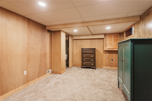 finished below grade area with light colored carpet, wood walls, visible vents, and a paneled ceiling