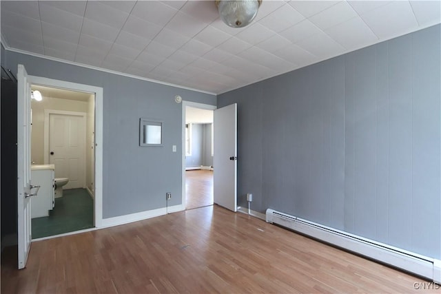 unfurnished bedroom featuring baseboard heating, ensuite bath, baseboards, wood finished floors, and a baseboard heating unit