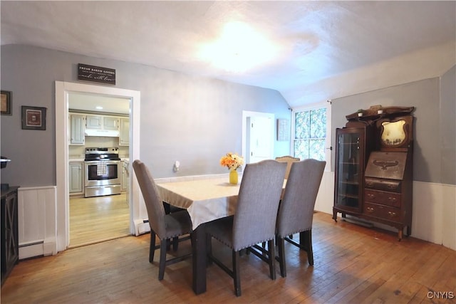 dining space with a baseboard radiator, light wood finished floors, vaulted ceiling, and baseboard heating