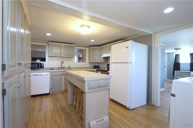 kitchen with light countertops, under cabinet range hood, a baseboard heating unit, a sink, and stainless steel appliances