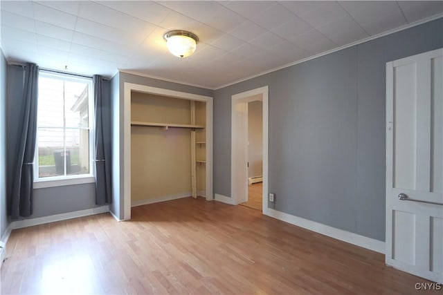 unfurnished bedroom featuring light wood-type flooring, baseboards, a baseboard radiator, a closet, and ornamental molding