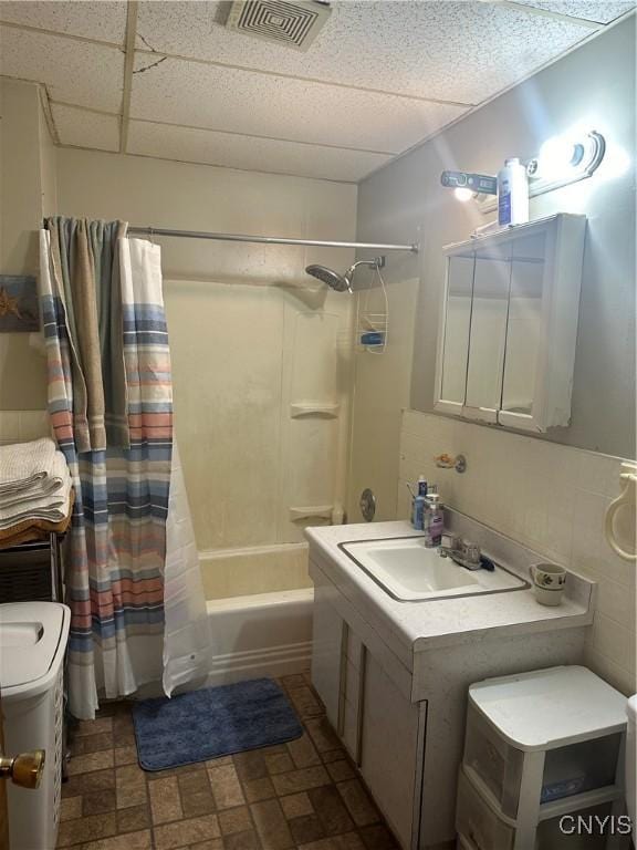 bathroom with vanity, toilet, shower / bath combination with curtain, a paneled ceiling, and visible vents