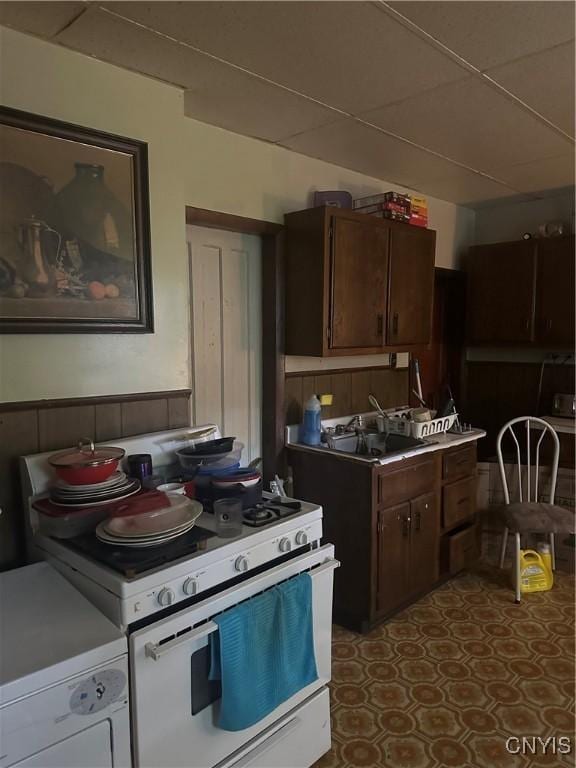 kitchen with dark brown cabinetry, a paneled ceiling, a sink, white range with gas cooktop, and washer / dryer