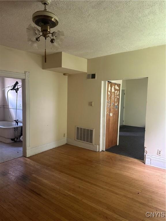unfurnished room with visible vents, baseboards, a textured ceiling, and wood finished floors