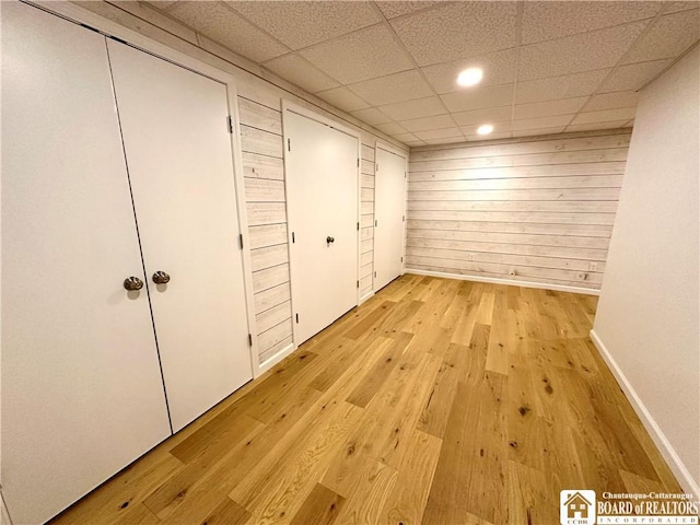 interior space with wooden walls, light wood-style floors, a paneled ceiling, recessed lighting, and baseboards