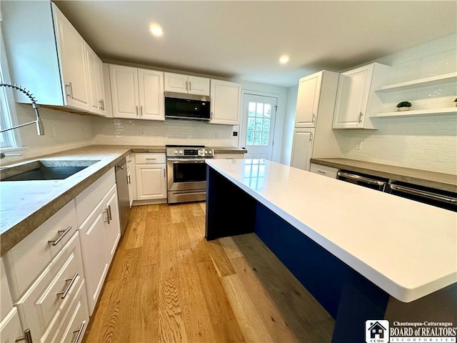 kitchen with appliances with stainless steel finishes, light wood-type flooring, a sink, and tasteful backsplash