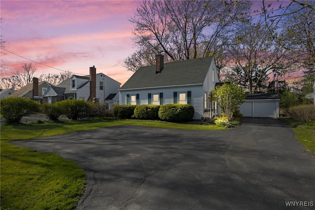 cape cod home featuring driveway, a chimney, a front yard, and a garage