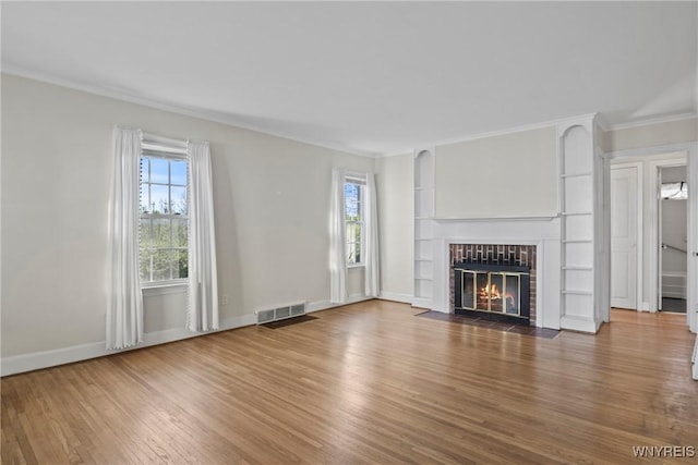 unfurnished living room featuring visible vents, ornamental molding, wood finished floors, baseboards, and a fireplace with flush hearth