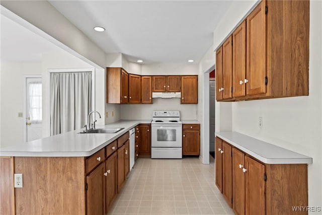 kitchen featuring white appliances, light countertops, under cabinet range hood, brown cabinets, and a sink