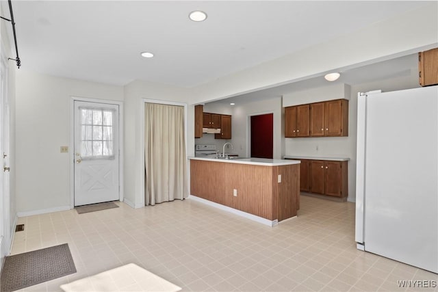 kitchen with light countertops, a sink, freestanding refrigerator, a peninsula, and under cabinet range hood