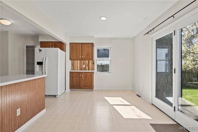 kitchen with light countertops, visible vents, brown cabinetry, and white refrigerator with ice dispenser