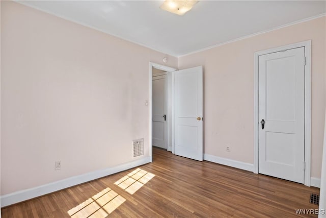 unfurnished bedroom featuring baseboards, ornamental molding, wood finished floors, and visible vents
