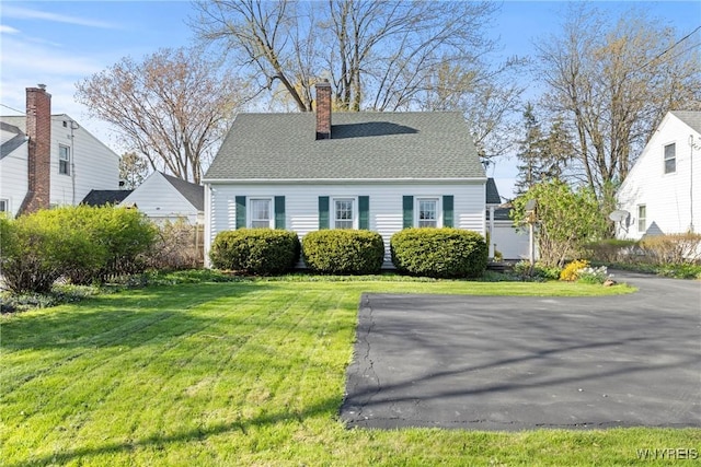 cape cod-style house featuring a shingled roof, a front lawn, and a chimney