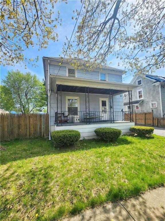 rear view of house featuring fence, covered porch, and a lawn