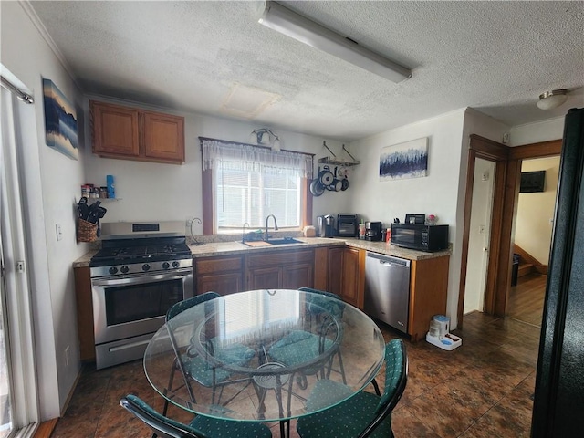 kitchen featuring a sink, a textured ceiling, appliances with stainless steel finishes, and brown cabinets