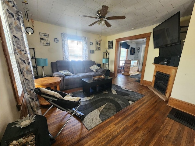 living room with a fireplace with raised hearth, a ceiling fan, visible vents, and hardwood / wood-style flooring