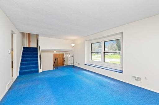 unfurnished living room featuring stairway, carpet, and visible vents